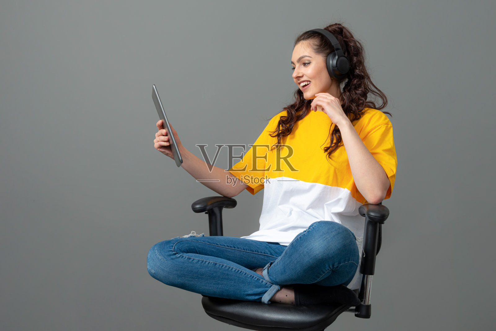 一名穿着黄色t恤的少年,一头卷发,坐在办公椅上使用平板电脑照片摄影图片