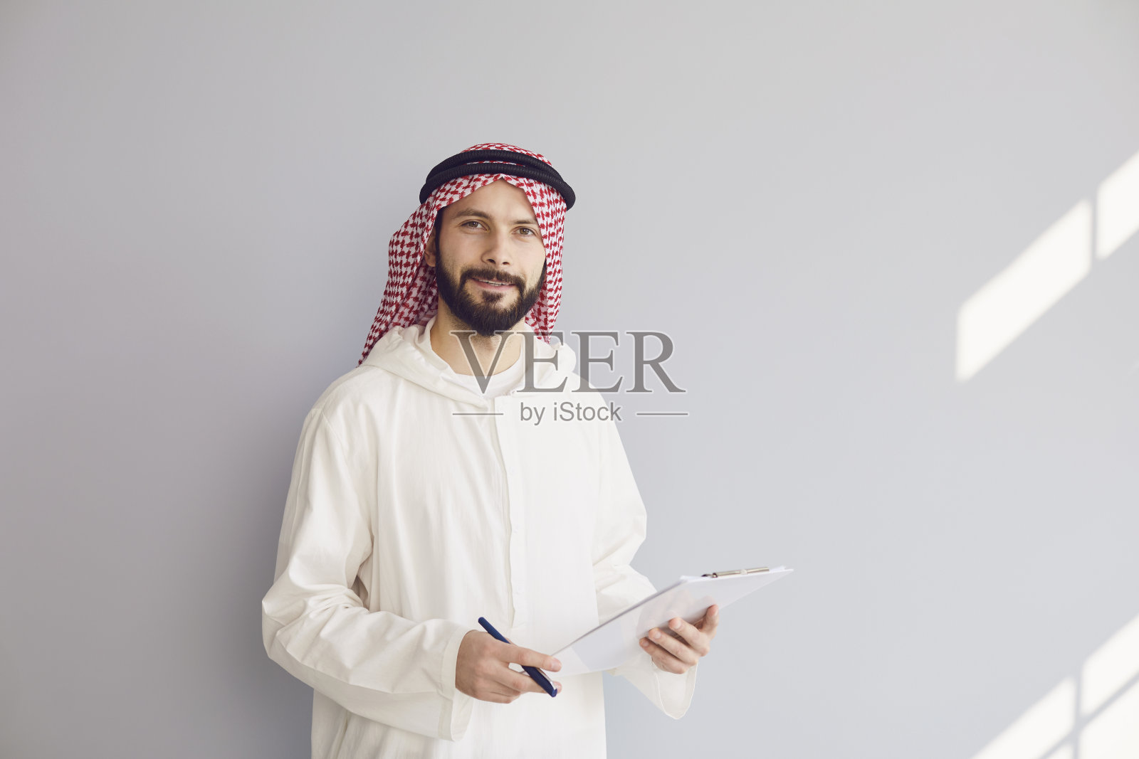 迷人微笑的阿拉伯男子在灰色背景的剪贴板上写字照片摄影图片