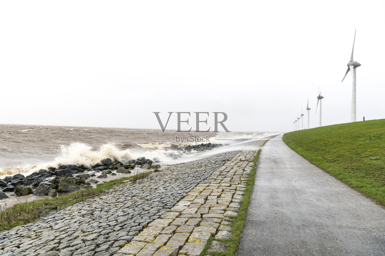 风力涡轮机在一个湖岸边与波浪冲击堤坝在暴风雨中照片摄影图片