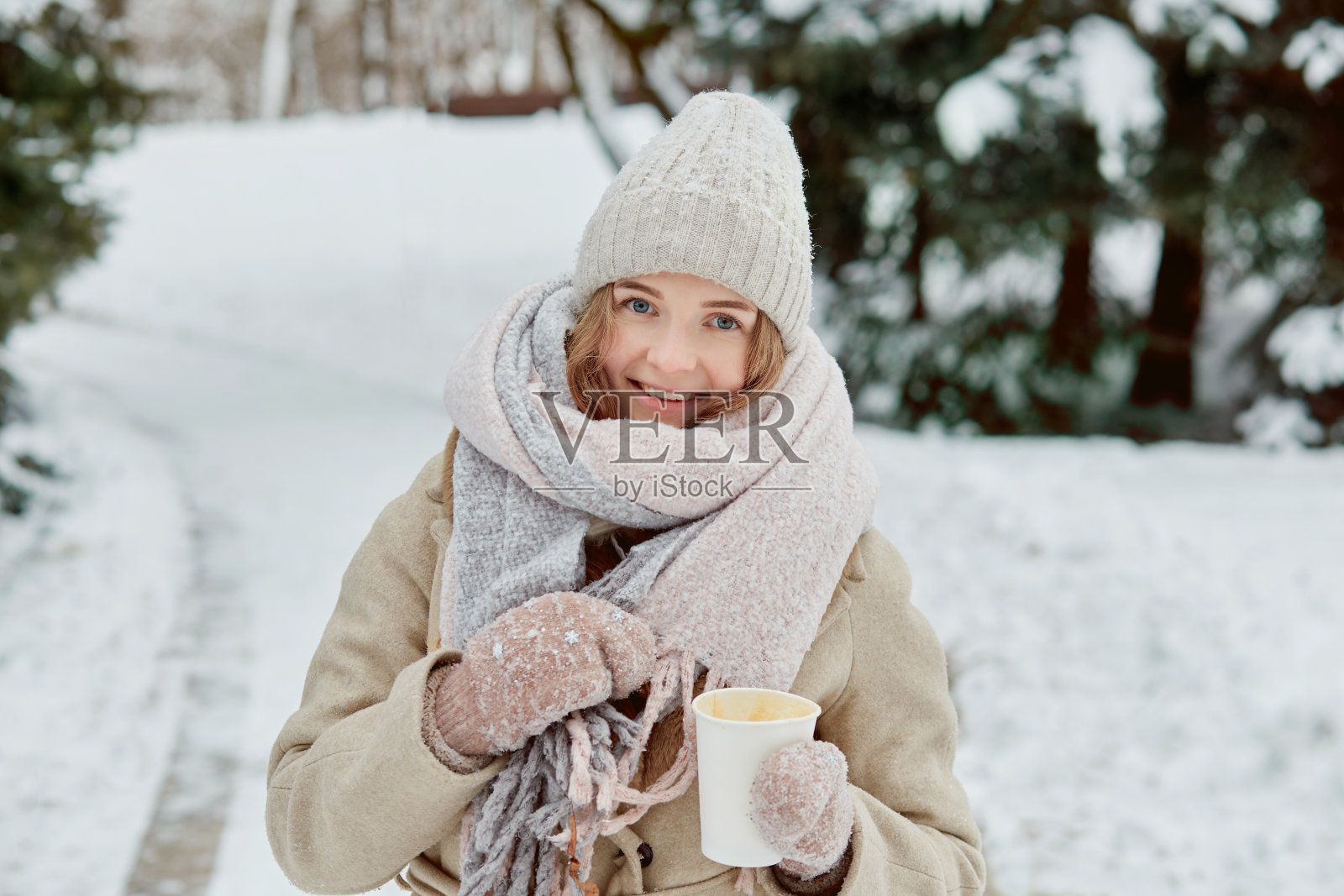 一个年轻的女人,戴着一顶编织的帽子,拿着一杯咖啡。照片摄影图片