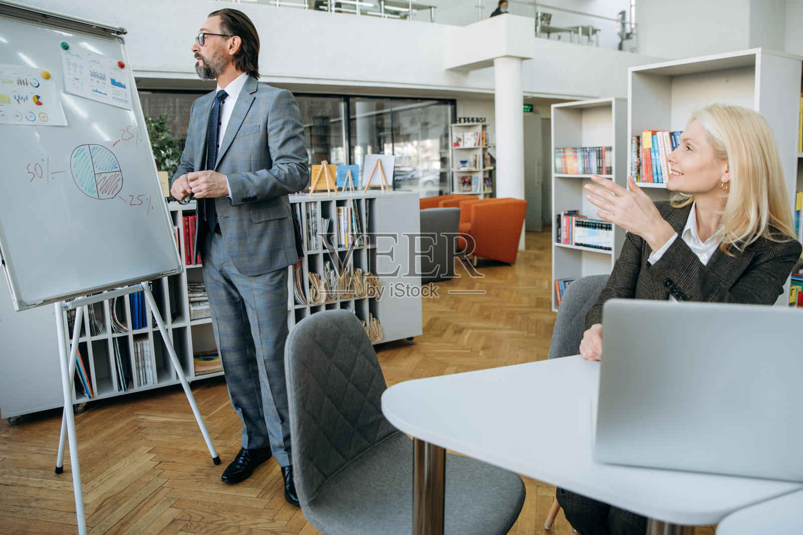 成功的商业同事讨论财务图表,公司每月利润。优雅的女老板穿着时尚的套装坐在办公桌前,听男同事发言照片摄影图片
