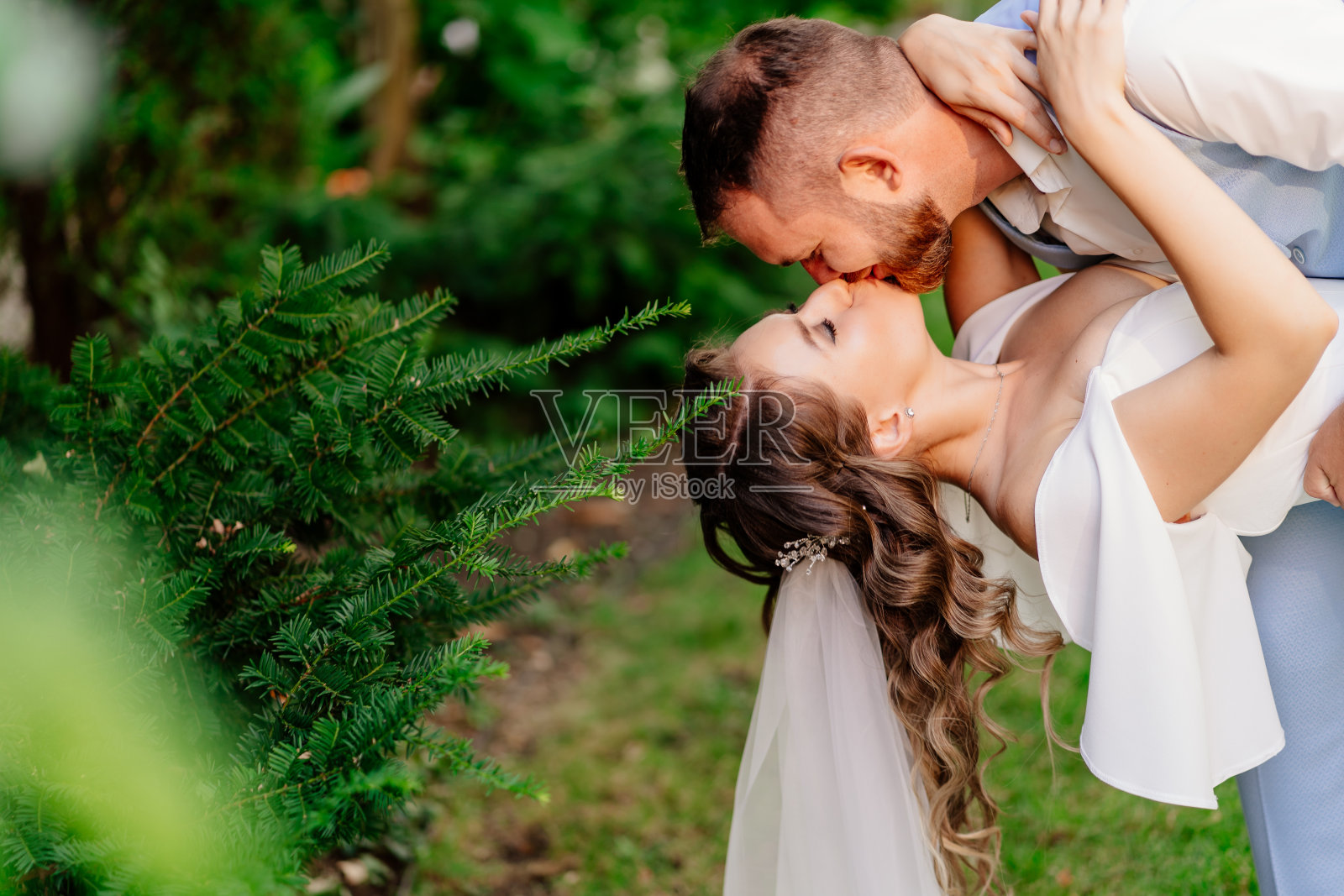 在公园里,新郎俯身与新娘共舞。在花园拍摄婚纱照。照片摄影图片