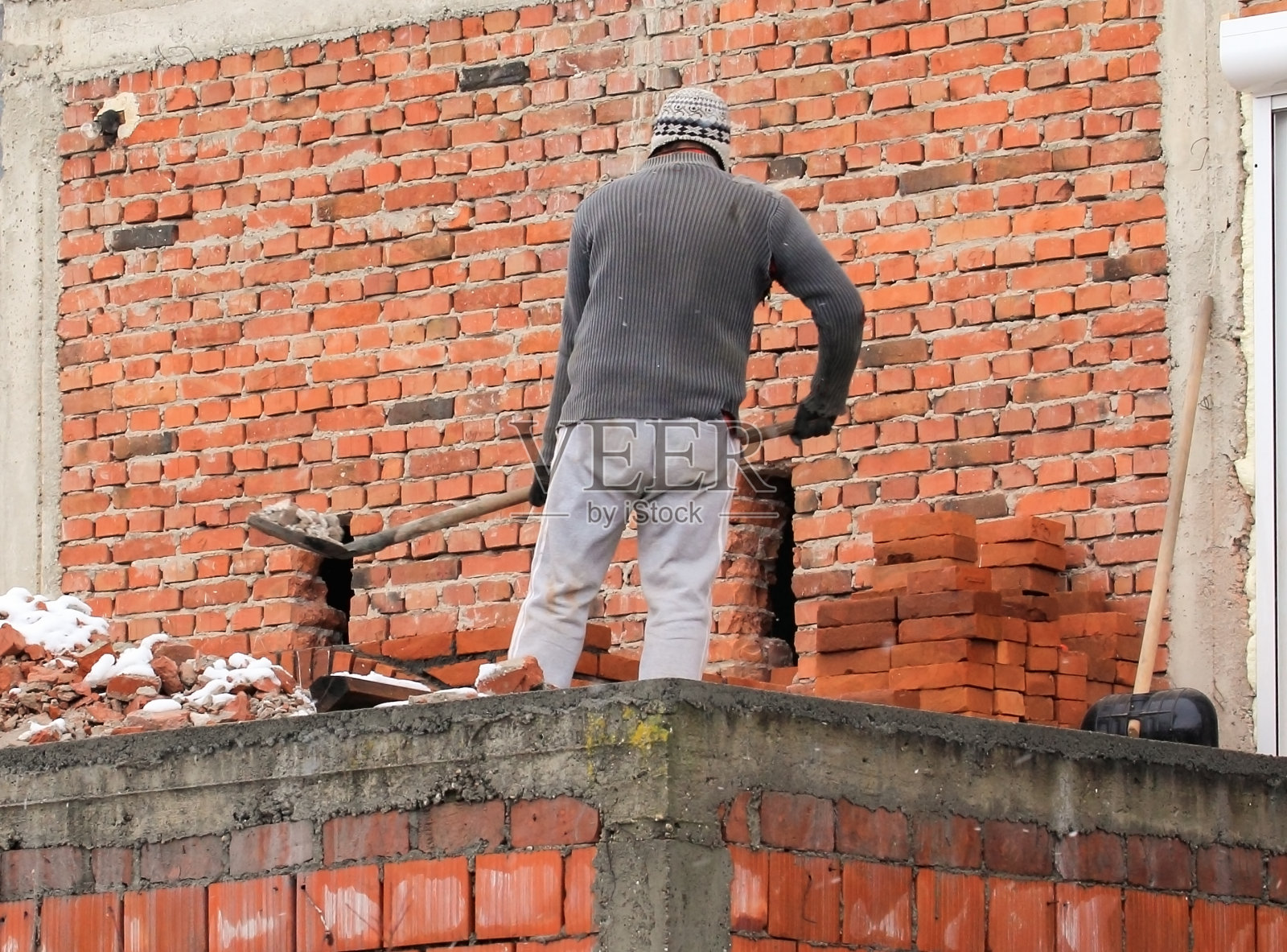 一名男子用铲子清除墙上钻了一个洞的碎片照片摄影图片