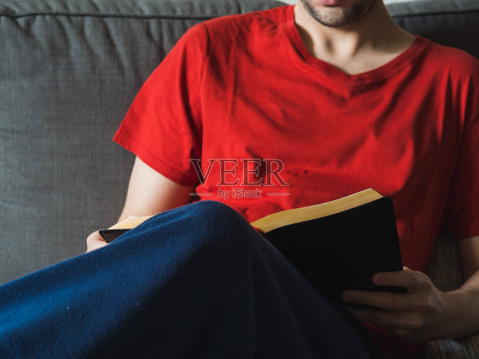一个穿着红色t恤的陌生人在沙发上看书照片摄影图片