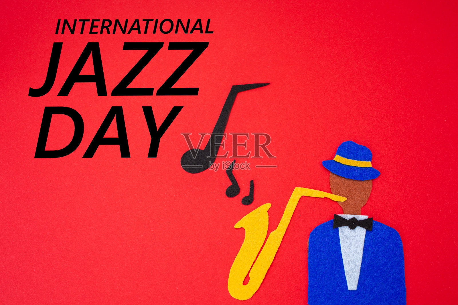 世界爵士的一天。用毛毡剪成的红色背景上,一个音乐家的剪影,手拿萨克斯管,旋律从里面飘出来。平躺照片摄影图片