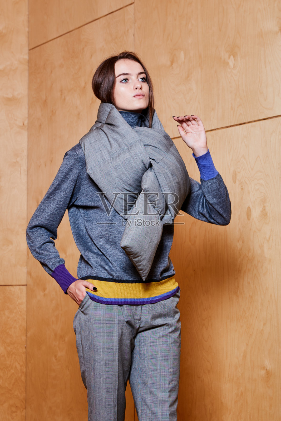 一个时尚的年轻女孩在一个胶合板背景的灰色裤子和灰色毛衣的工作室肖像照片摄影图片