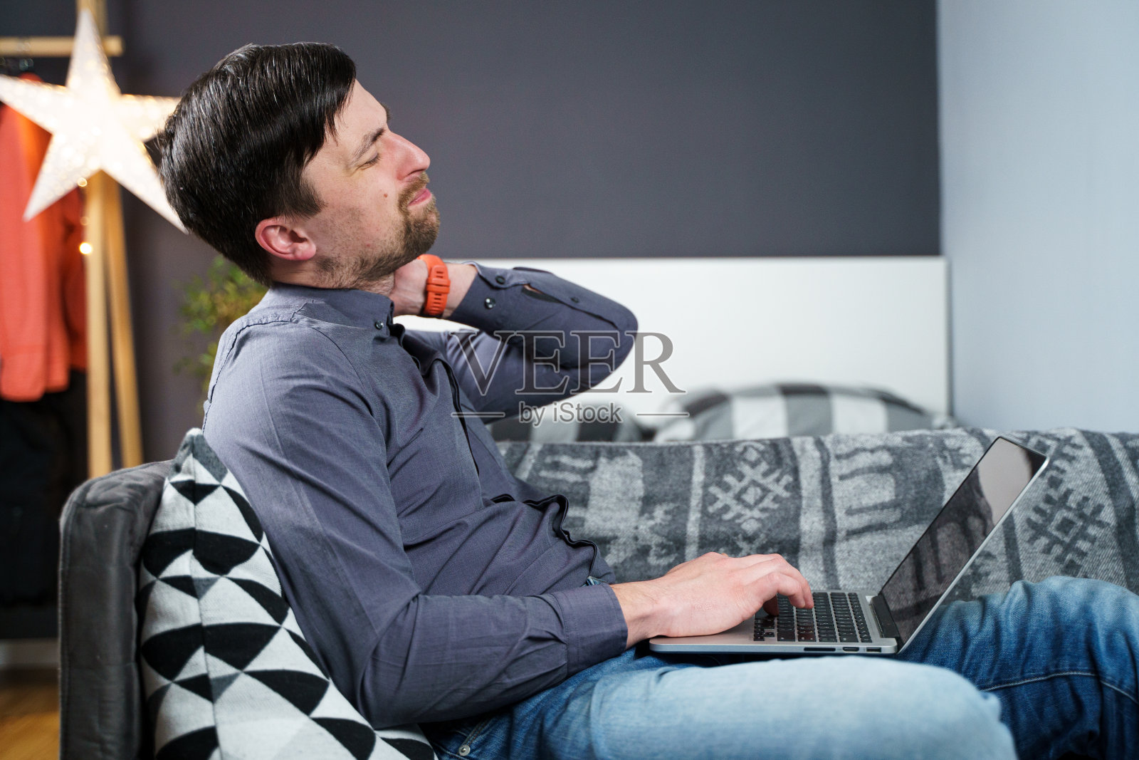 男员工意外在家工作后在笔记本电脑后感到颈部疼痛,用黑色项圈支撑。颈部受伤的男性自由程序员请病假在沙发上的电脑前工作照片摄影图片