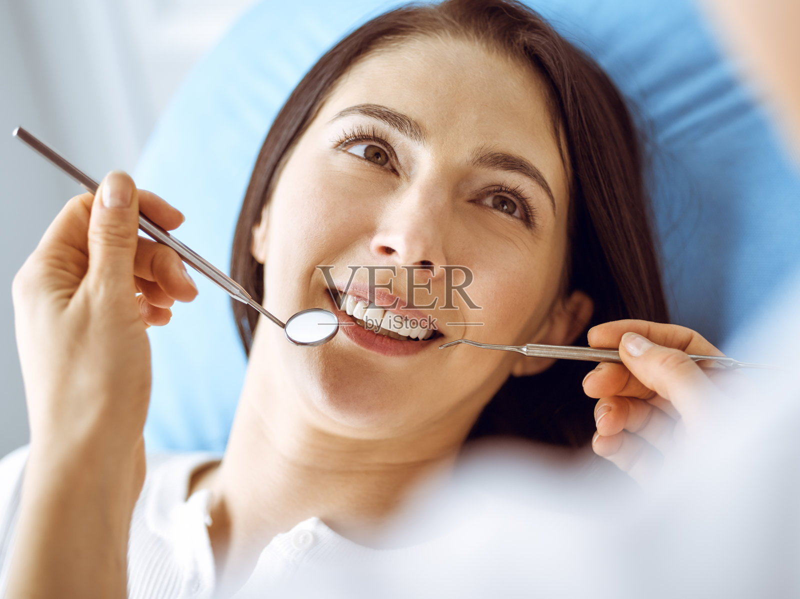 微笑的黑发女人正在检查牙医在牙科诊所。医生的手拿着牙科器械靠近病人的嘴。健康牙齿和医学理念照片摄影图片