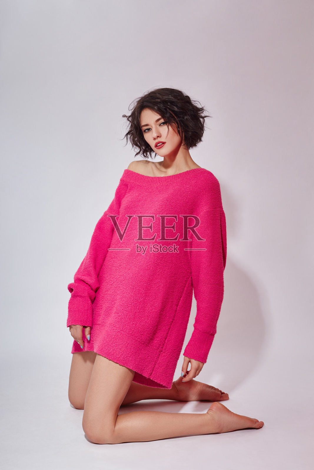 黑发短发的女人穿着粉红色的毛衣在白色的背景上摆姿势。经典的女性亮妆照片摄影图片