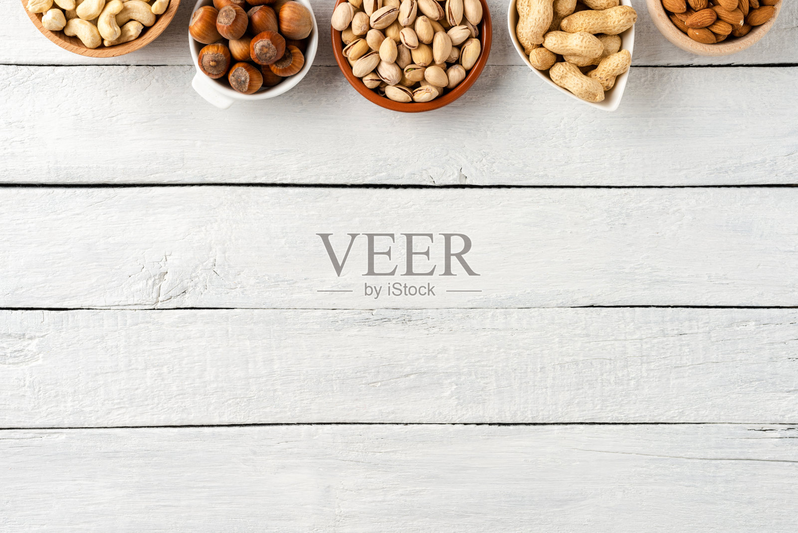 头顶拍摄的不同坚果碗在白色木制背景与copyspace。近距离照片摄影图片