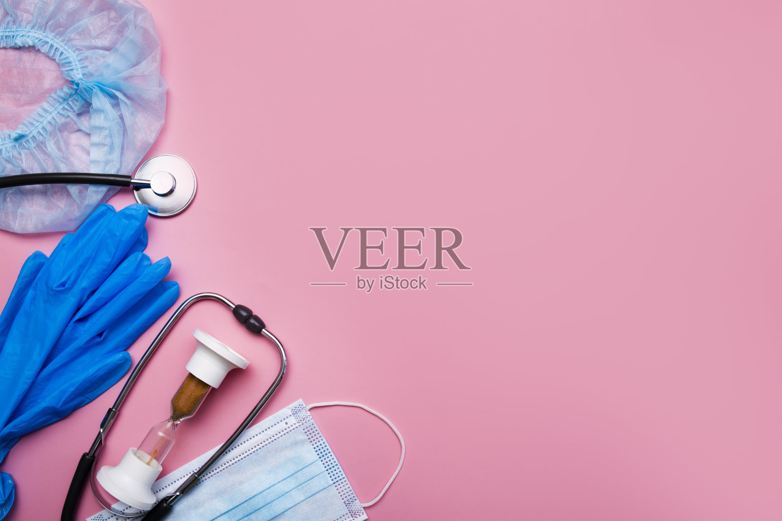 注射器,手套,防护口罩,沙漏,听诊器,粉红色背景,有拷贝空间。照片摄影图片