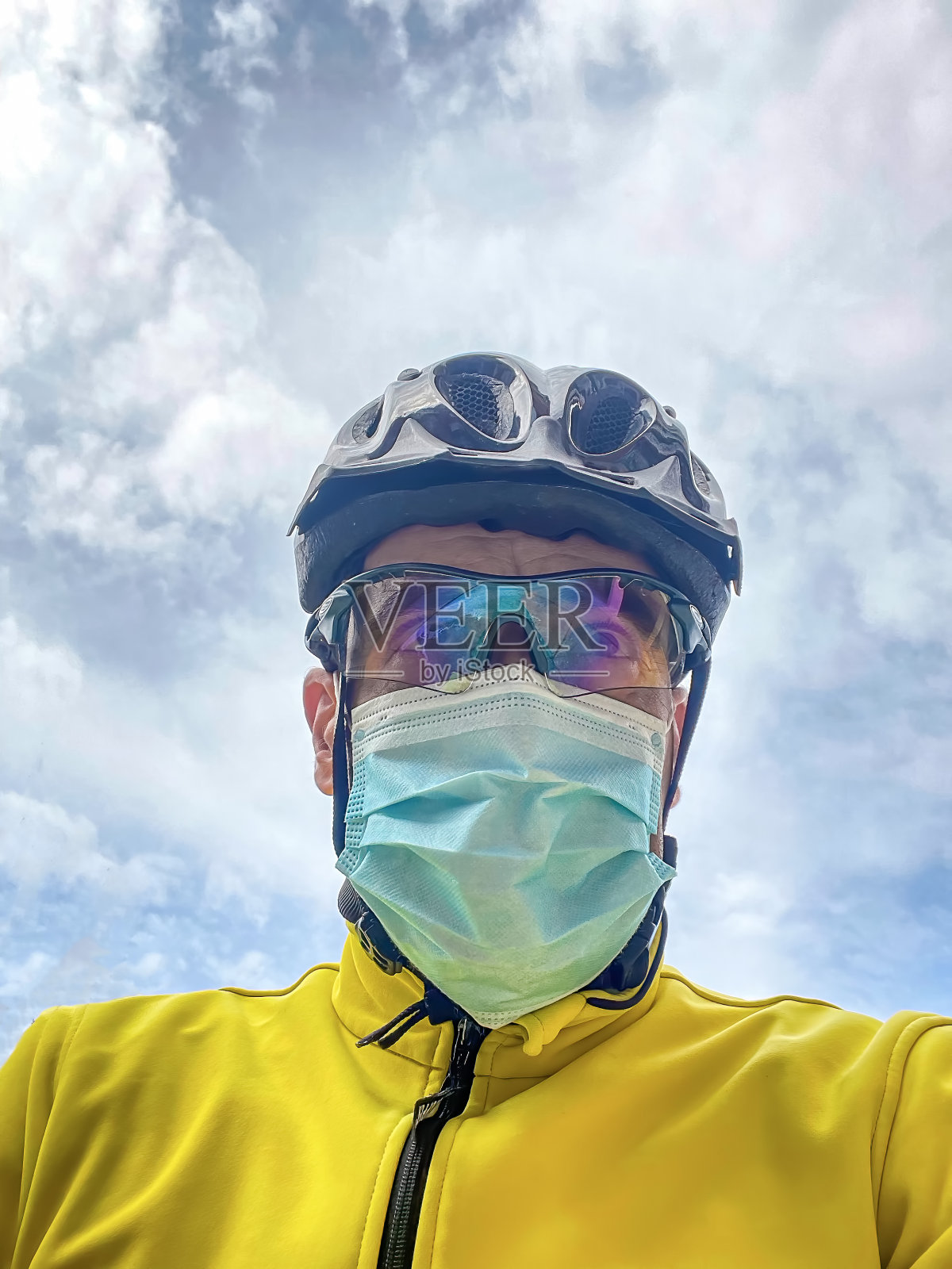 一个骑自行车的人戴着头盔,眼镜和一件黄色的夹克,骑着一辆带着面具的自行车照片摄影图片