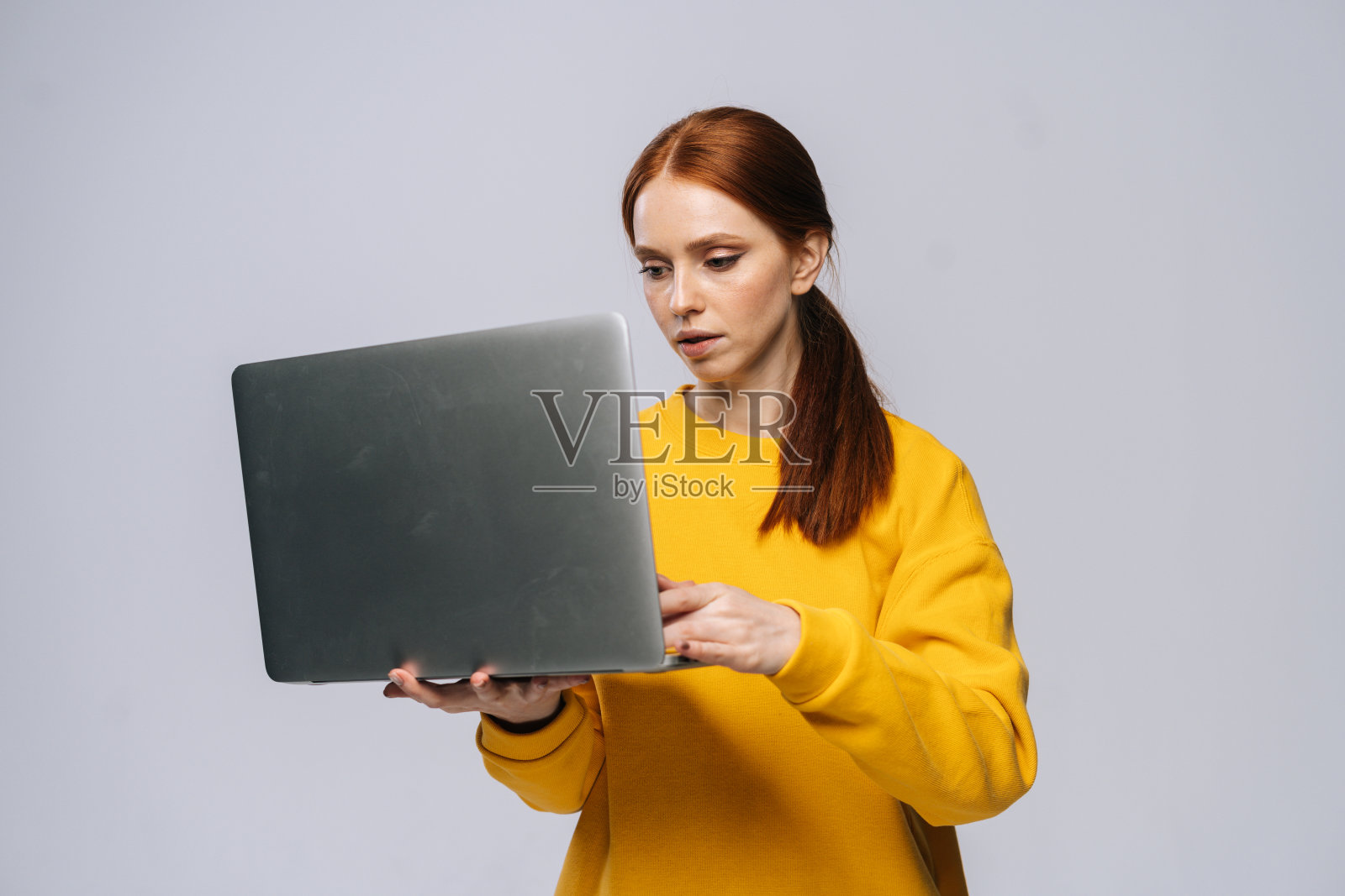 成功的年轻女学生手持笔记本电脑,在孤立的灰色背景上打字。照片摄影图片