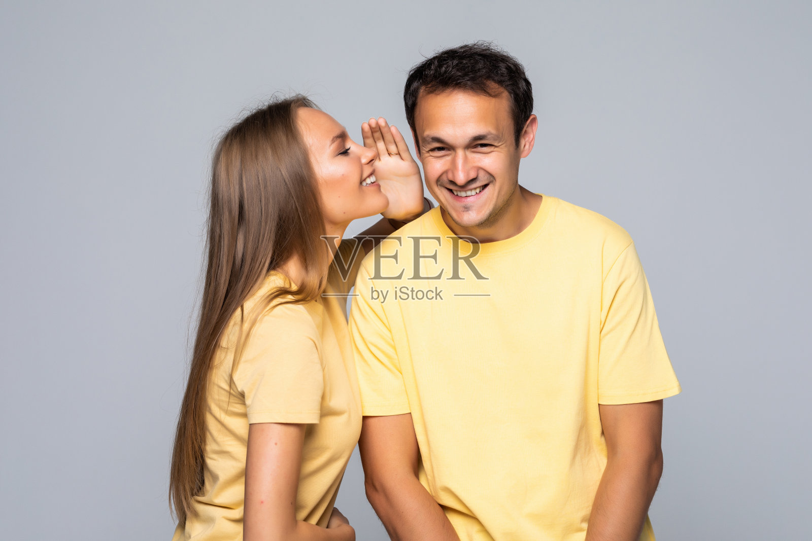 秘密与人的概念。一对幸福的夫妇在灰色的背景下窃窃私语照片摄影图片