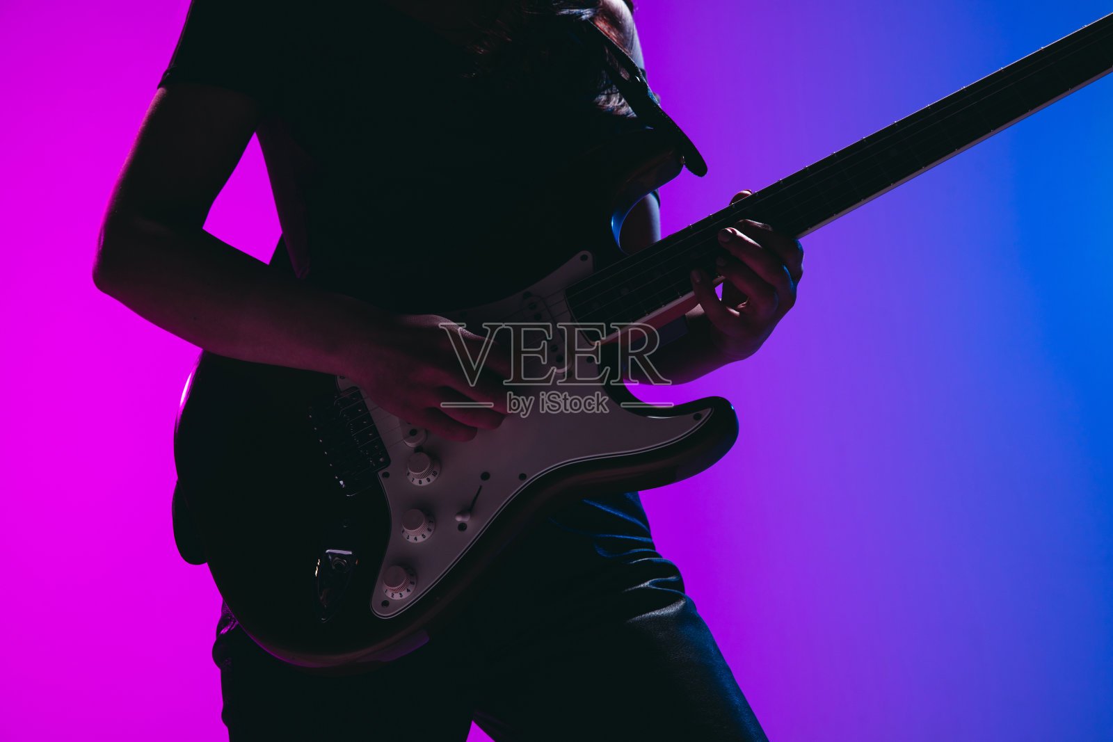 剪影的年轻女吉他手孤立在蓝粉色的背景霓虹灯。照片摄影图片