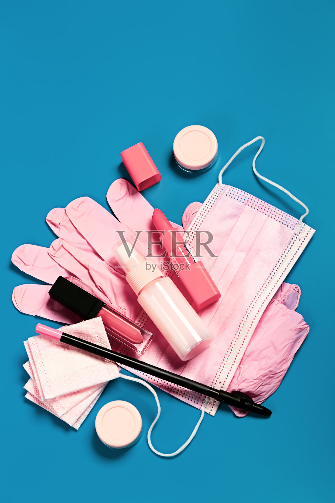 女性保护旅行化妆包套装。粉色面膜、手套、消毒液、唇胶、铅笔和口红,蓝色底色。照片摄影图片
