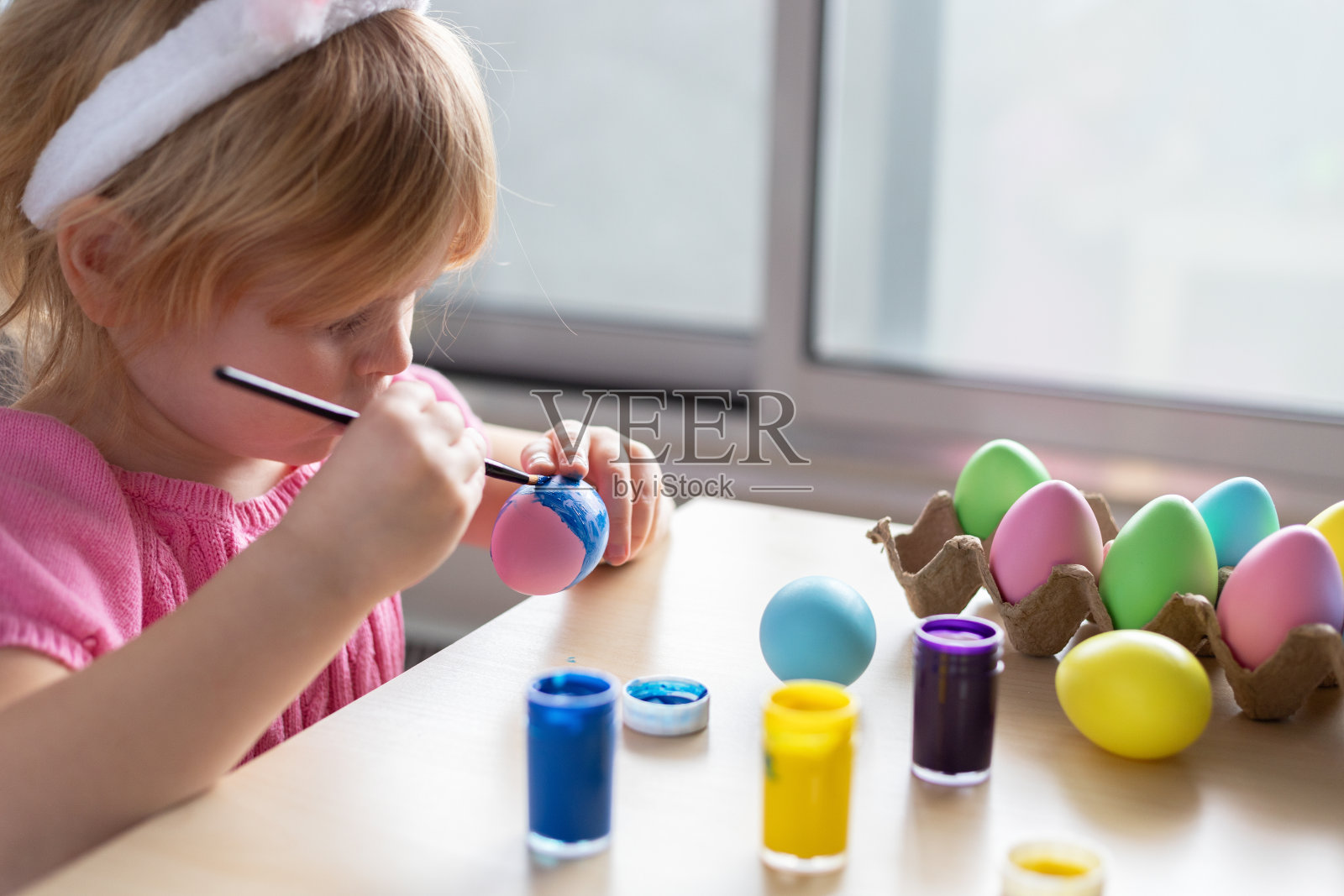 小女孩在复活节兔子的耳朵里画彩蛋。照片摄影图片