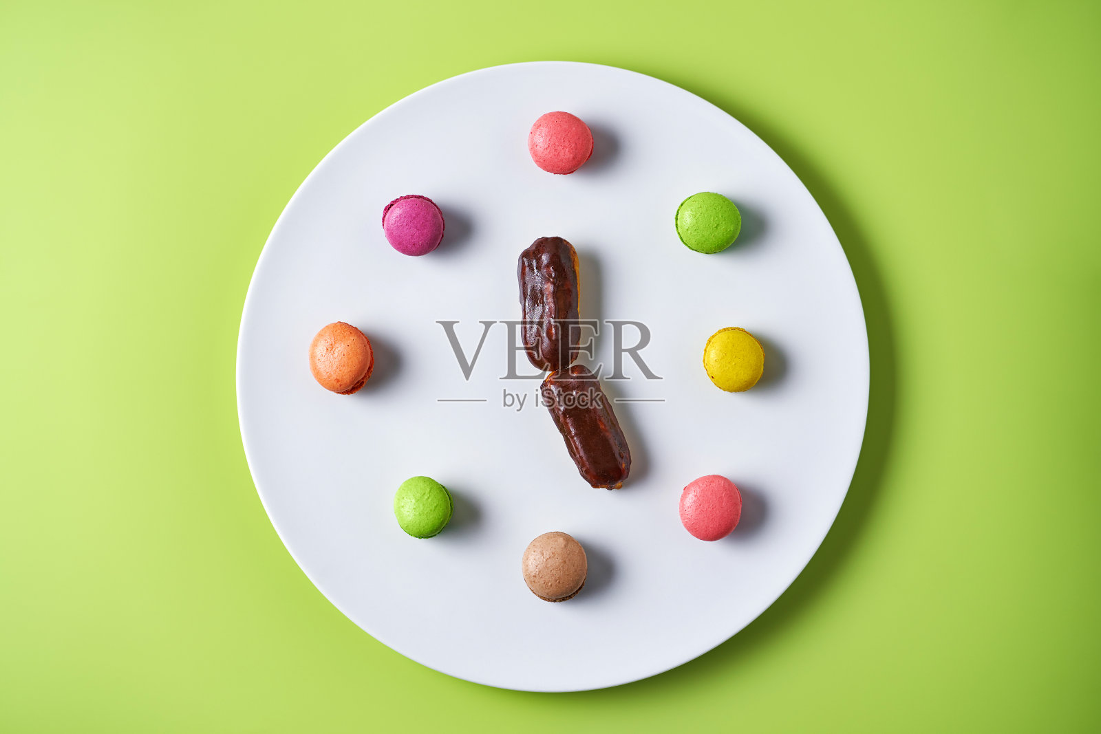 马卡龙和清亮的白色盘子显示5点钟在浅绿色的背景照片摄影图片