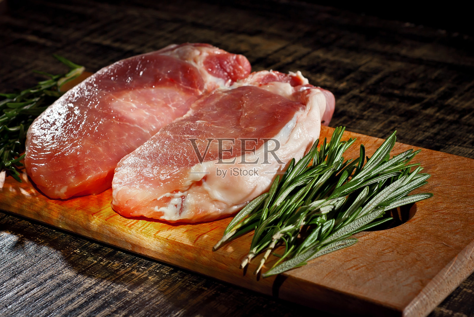 黑底木板上的生牛排。破旧的桌子上放着红肉。作为一种艺术效果来对比戏剧性的光线。照片摄影图片