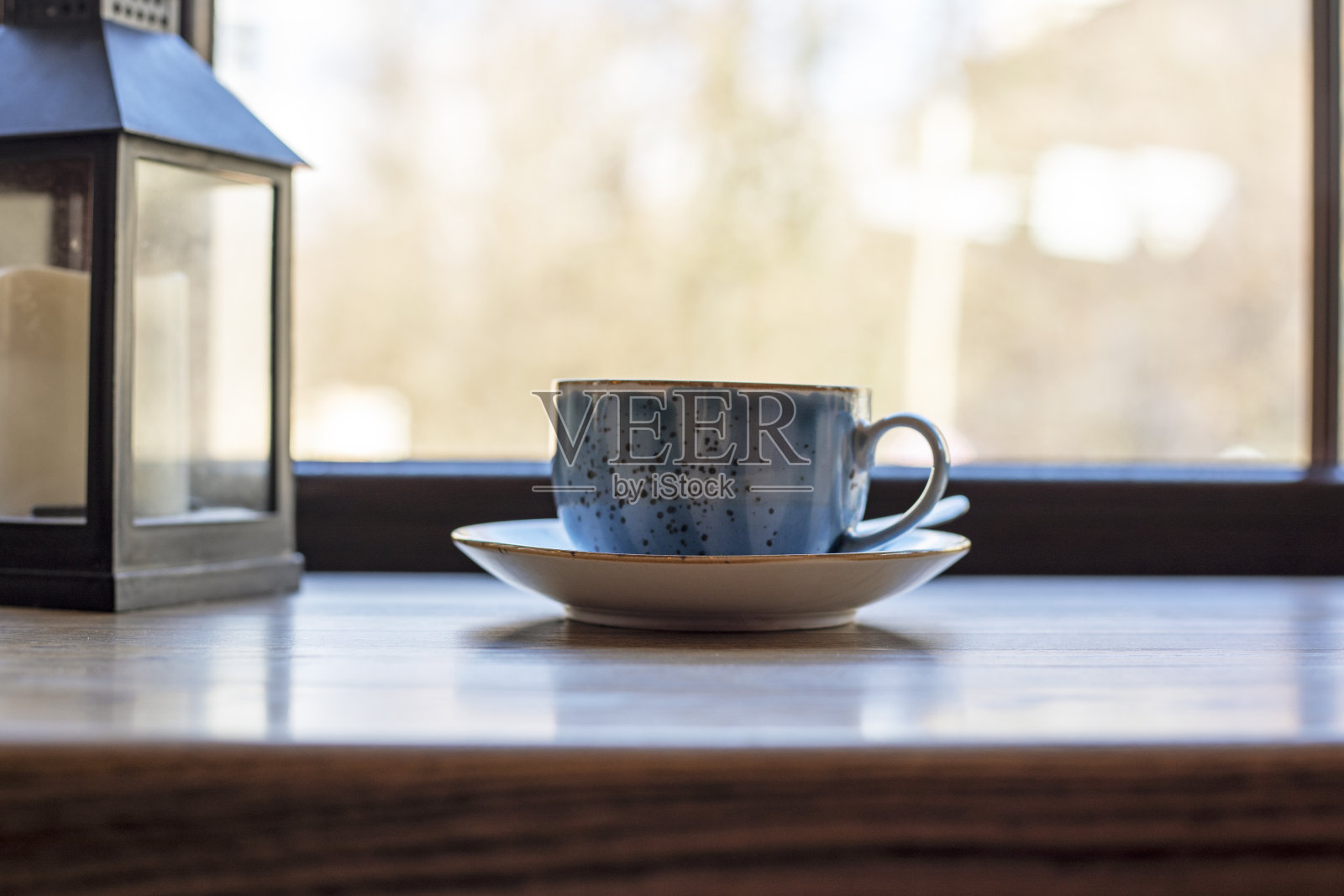 蓝色的杯子a在桌子上,白天的背景是窗户。照片摄影图片