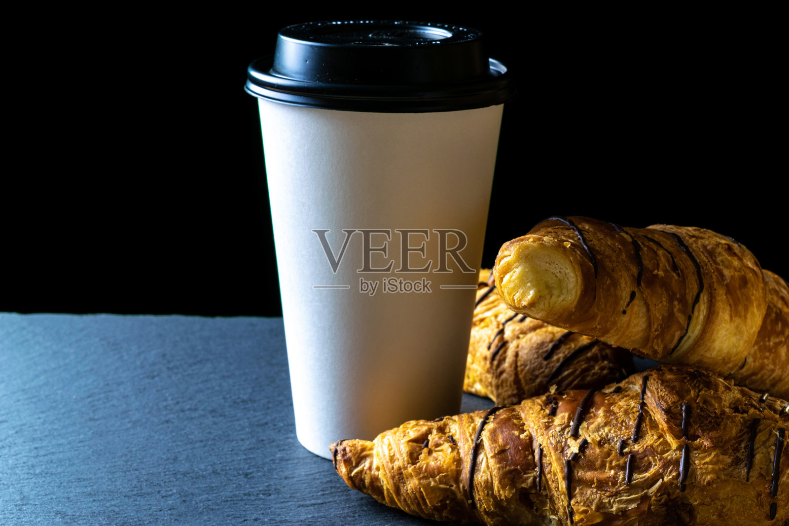 羊角面包纹理。法式早餐牛角面包,新鲜的糕点面包与纸咖啡杯在面包店在黑色的石头背景。面包烘焙产品咖啡概念。照片摄影图片