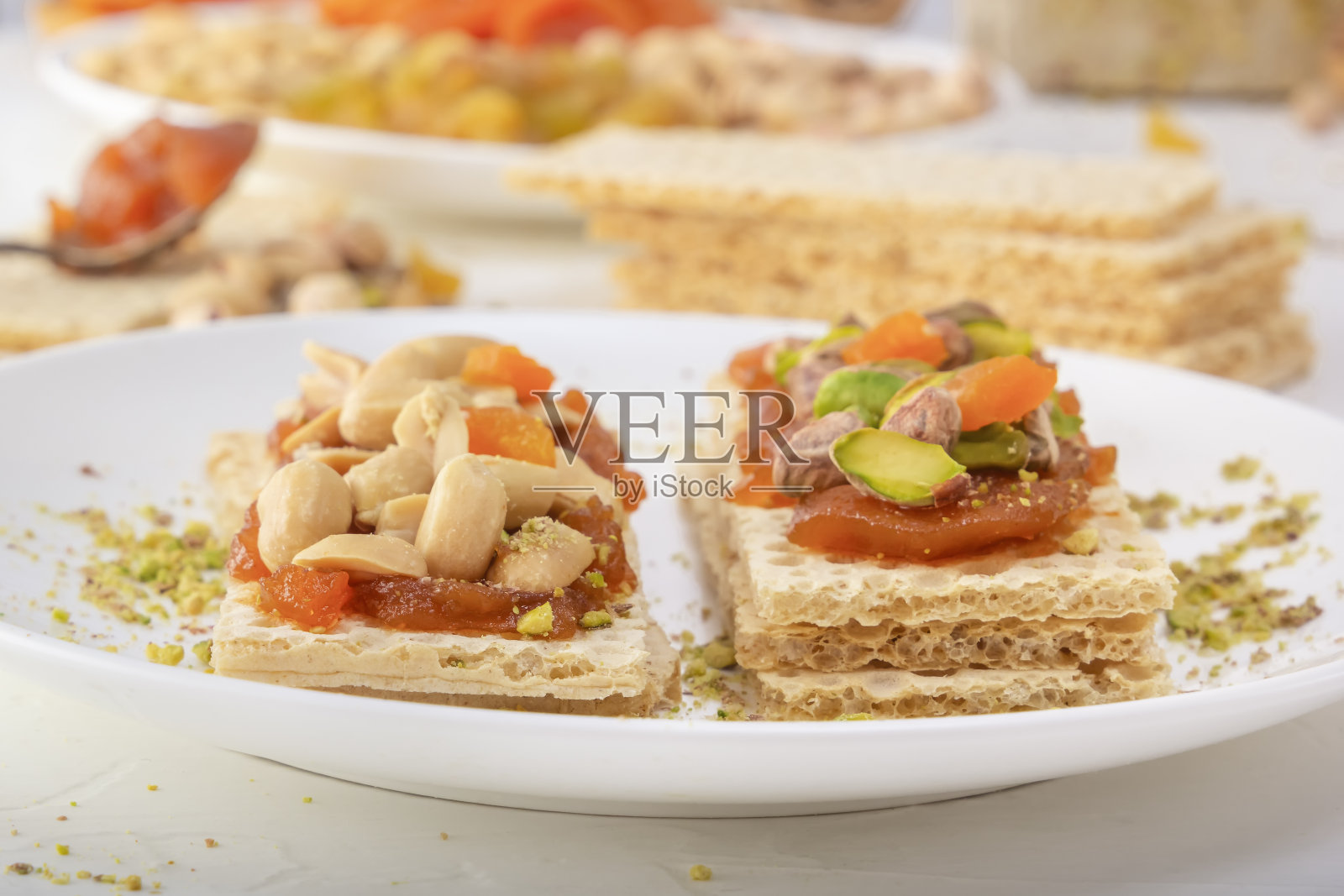 白色的盘子上放着一层薄薄的杏酱,上面放着花生、开心果、葡萄干和蜜饯水果,背景是东方糖果。照片摄影图片