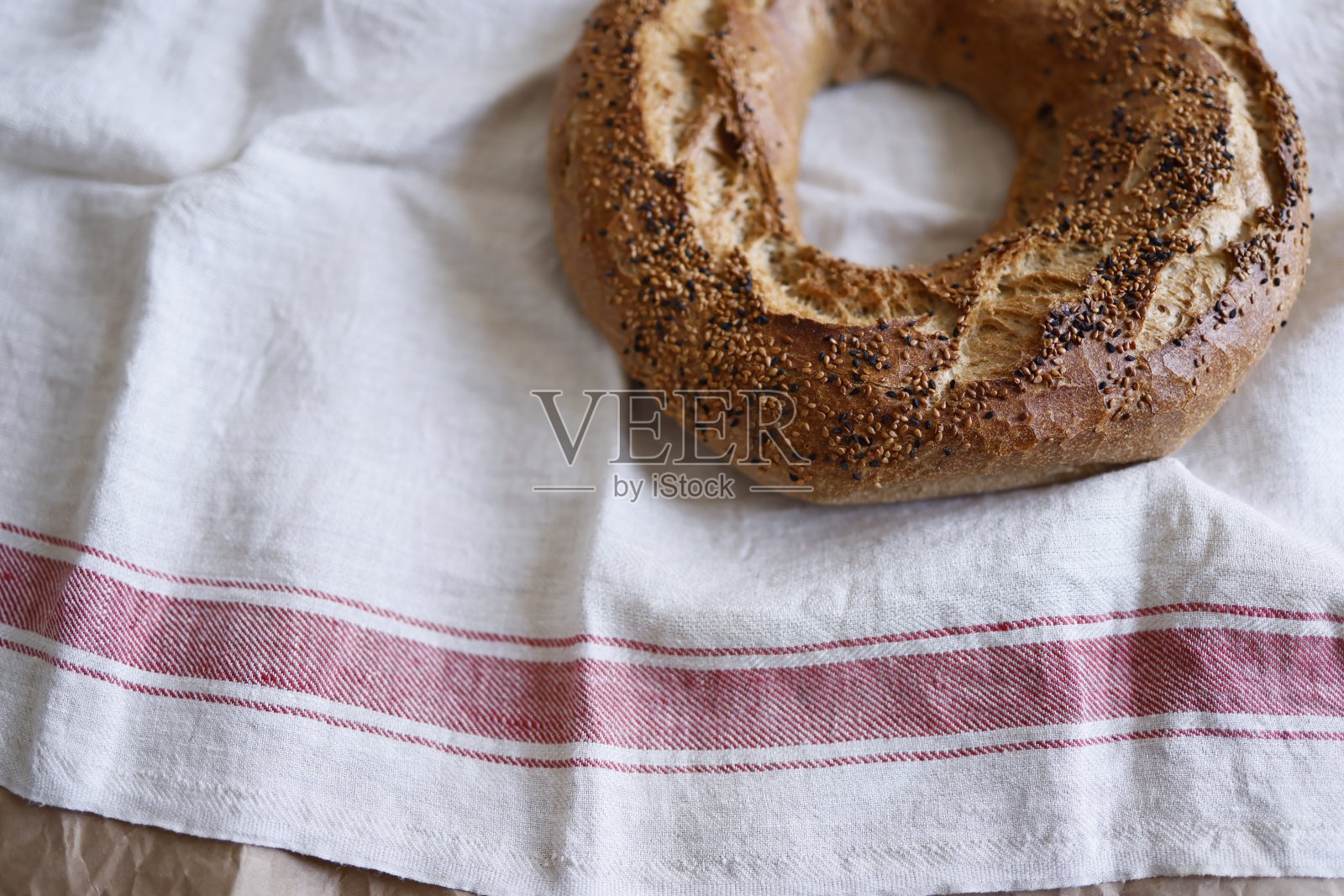 一段百吉饼面包与芝麻和黑孜然在米色亚麻布覆盖与红色条纹在边缘,脆百吉饼面包照片摄影图片