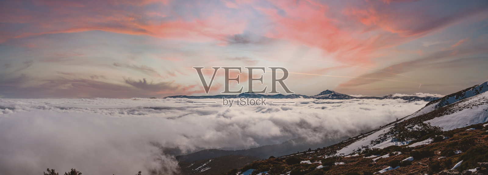 日落时,雪山覆盖在云上的全景照片摄影图片