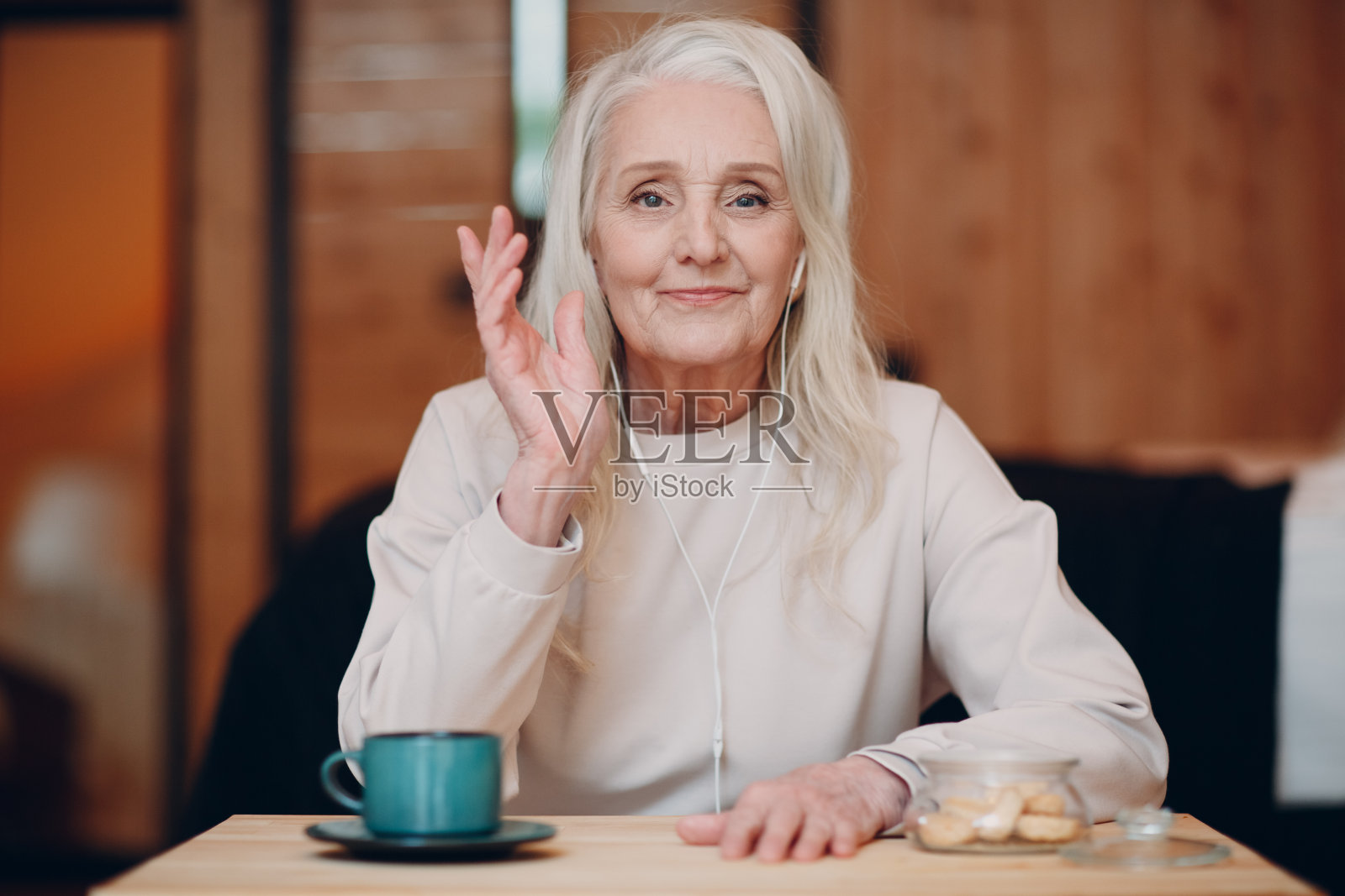 老年妇女用耳机在厨房的笔记本电脑上进行视频通话,对着屏幕挥手,聊天和说话的摄像设备视图照片摄影图片