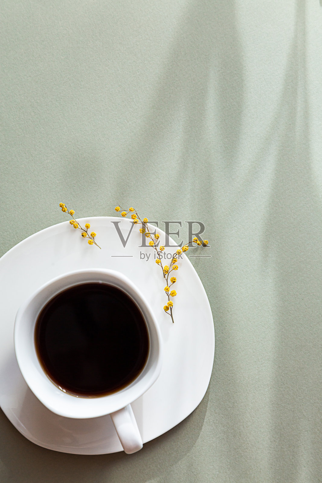 极简主义的春天静物生活。白杯黑咖啡,淡绿色背景上的长长的阴影。副本的空间。照片摄影图片