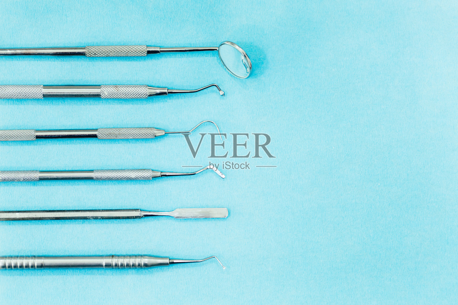 蓝色背景上的牙科器械。牙科治疗和牙科卫生。牙医的工具,镜子,钩子,刮刀。用于复制和文本的空间照片摄影图片
