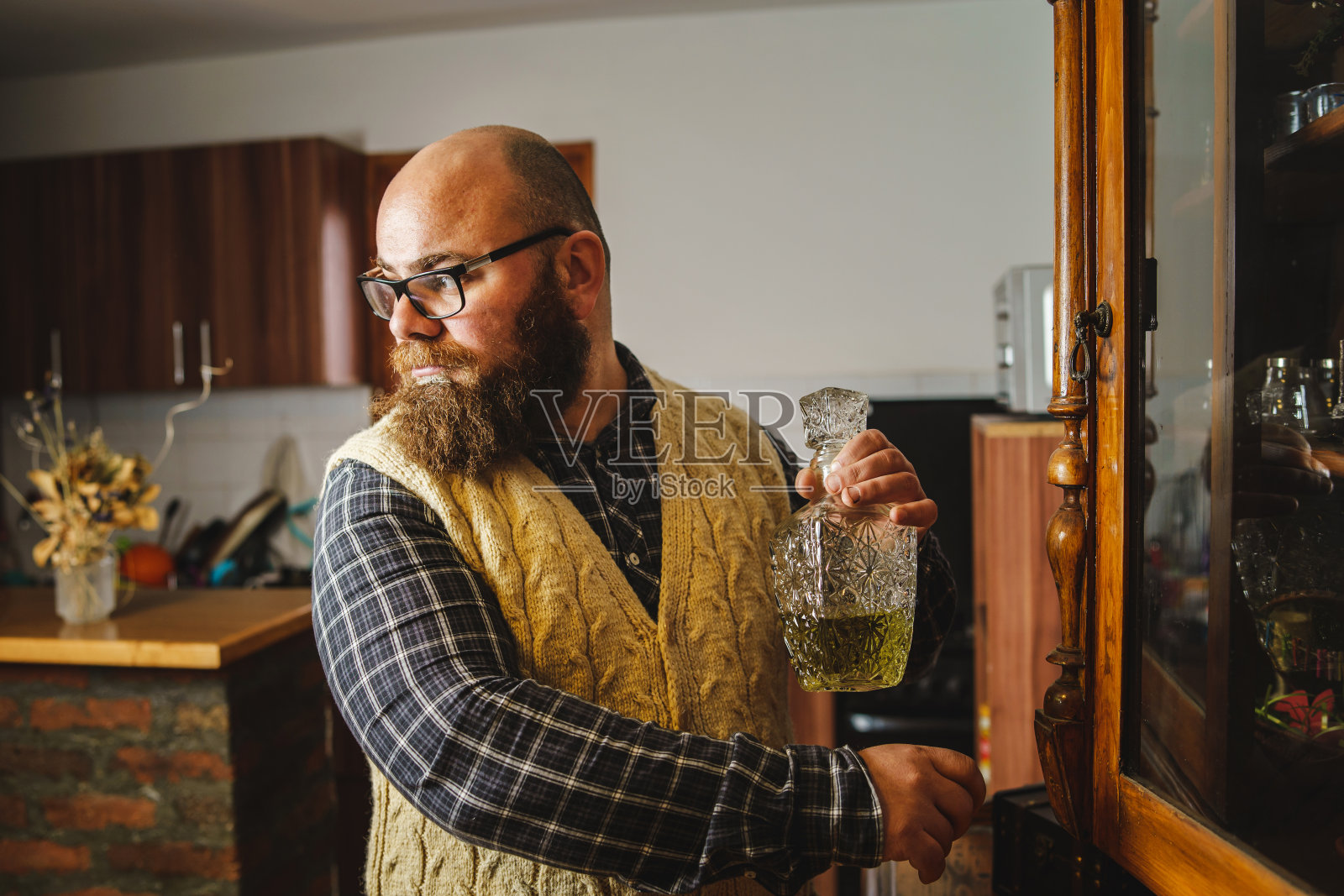 侧面的观点,大胆和胡子白种人拿着一瓶白兰地rakija在家里看,如果有人在看他照片摄影图片
