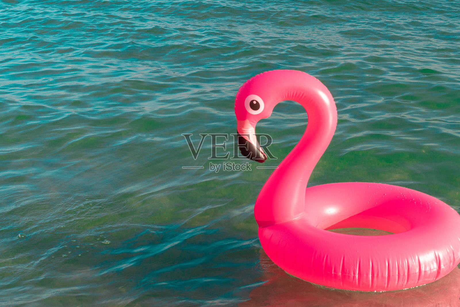 夏天有趣的海滩。粉红色的充气火烈鸟在蓝色的海水在夏季海洋海滩的背景。有趣的小鸟玩具的孩子。照片摄影图片