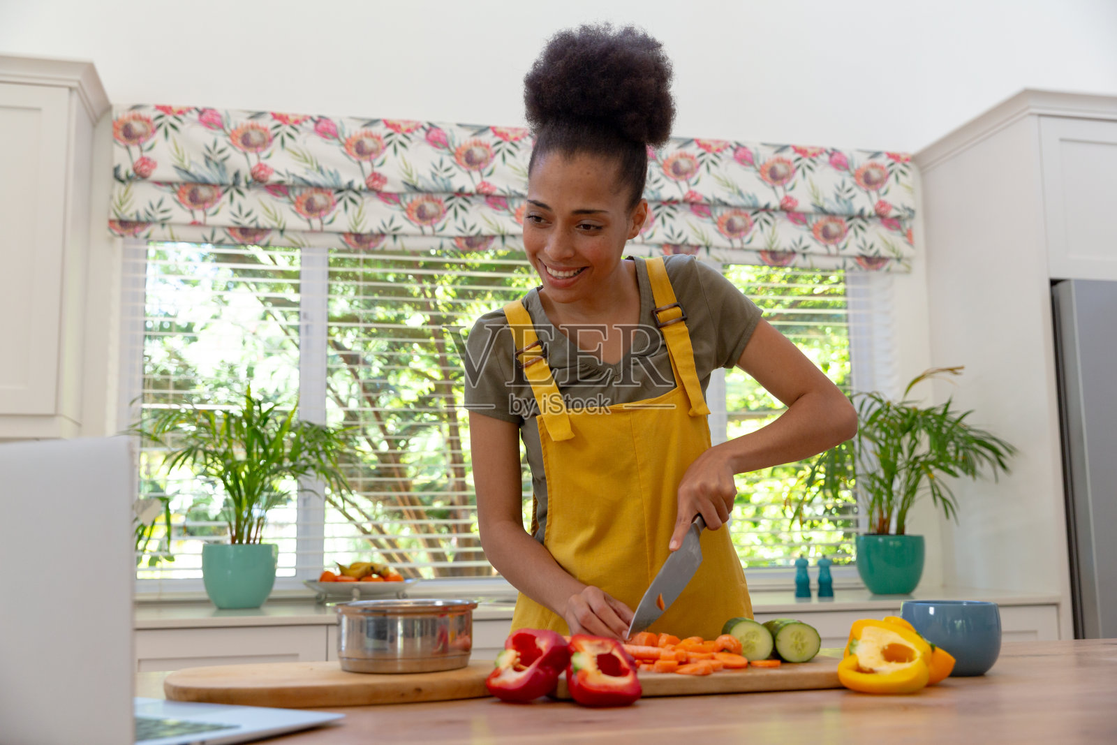 混血妇女在厨房里微笑着用笔记本电脑切菜照片摄影图片