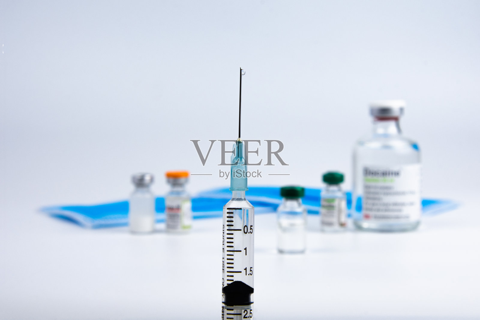 关闭装有covid-19疫苗的模糊瓶子上的注射器,白色背景。用于预防COVID-19的新型冠状病毒疫苗的小瓶。医疗保健和医疗理念。照片摄影图片