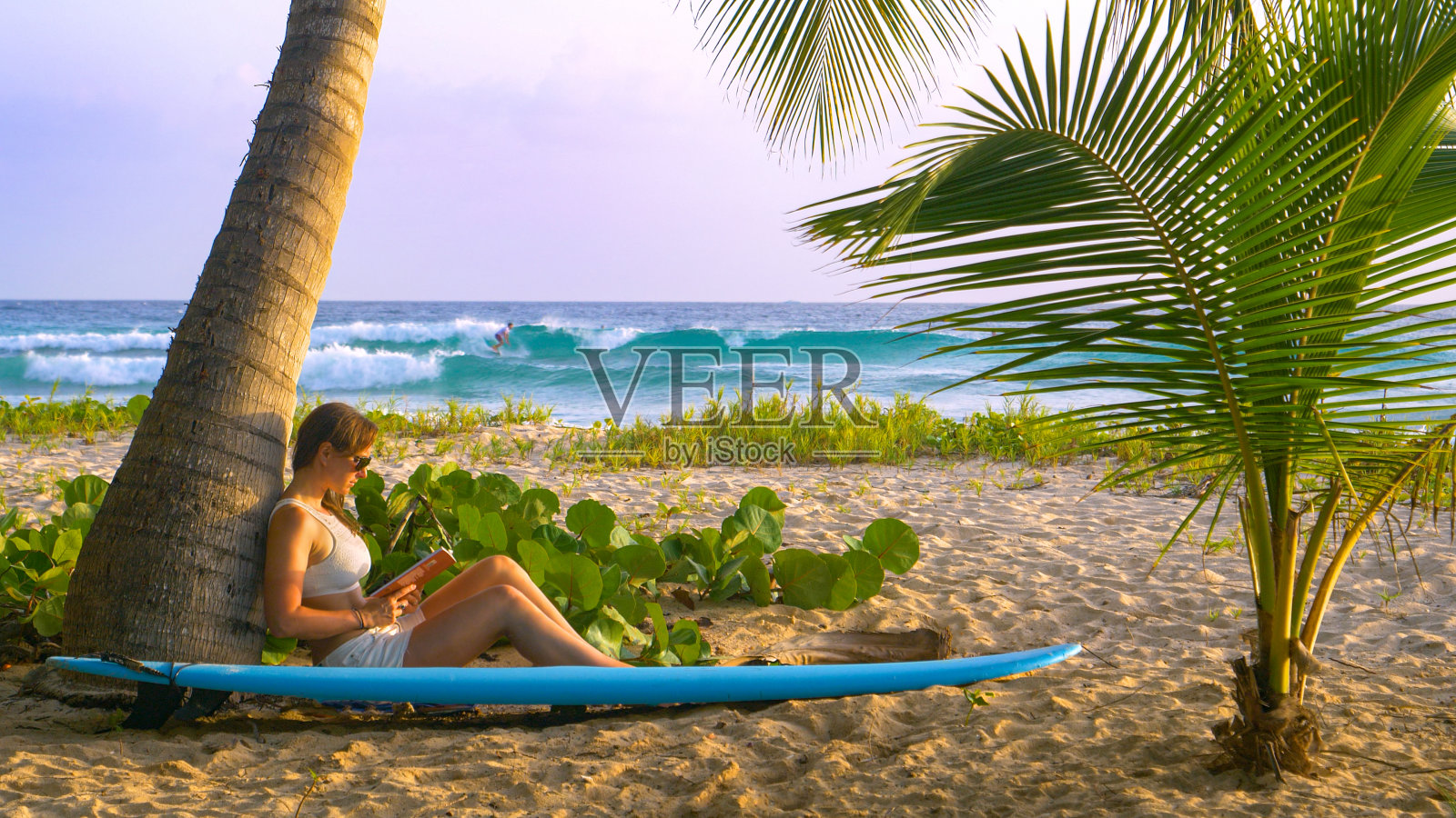 特写:女人在一个受欢迎的冲浪点附近的海滩上放松,并读一本书。照片摄影图片