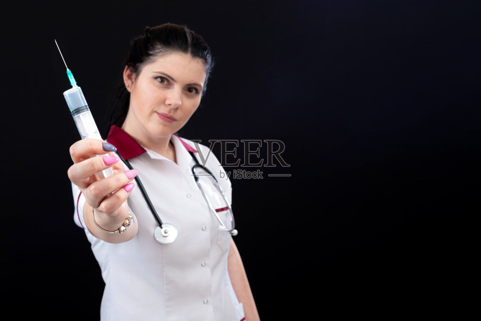 医学、疫苗接种和保健概念,深色背景下带着听诊器和注射器的女医生特写照片摄影图片