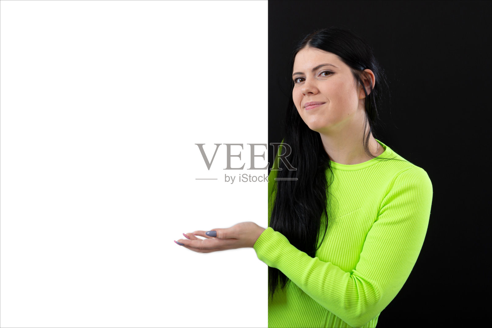 迷人的黑发女子在鲜艳的衣服与白色空白海报,孤立在一个黑暗照片摄影图片