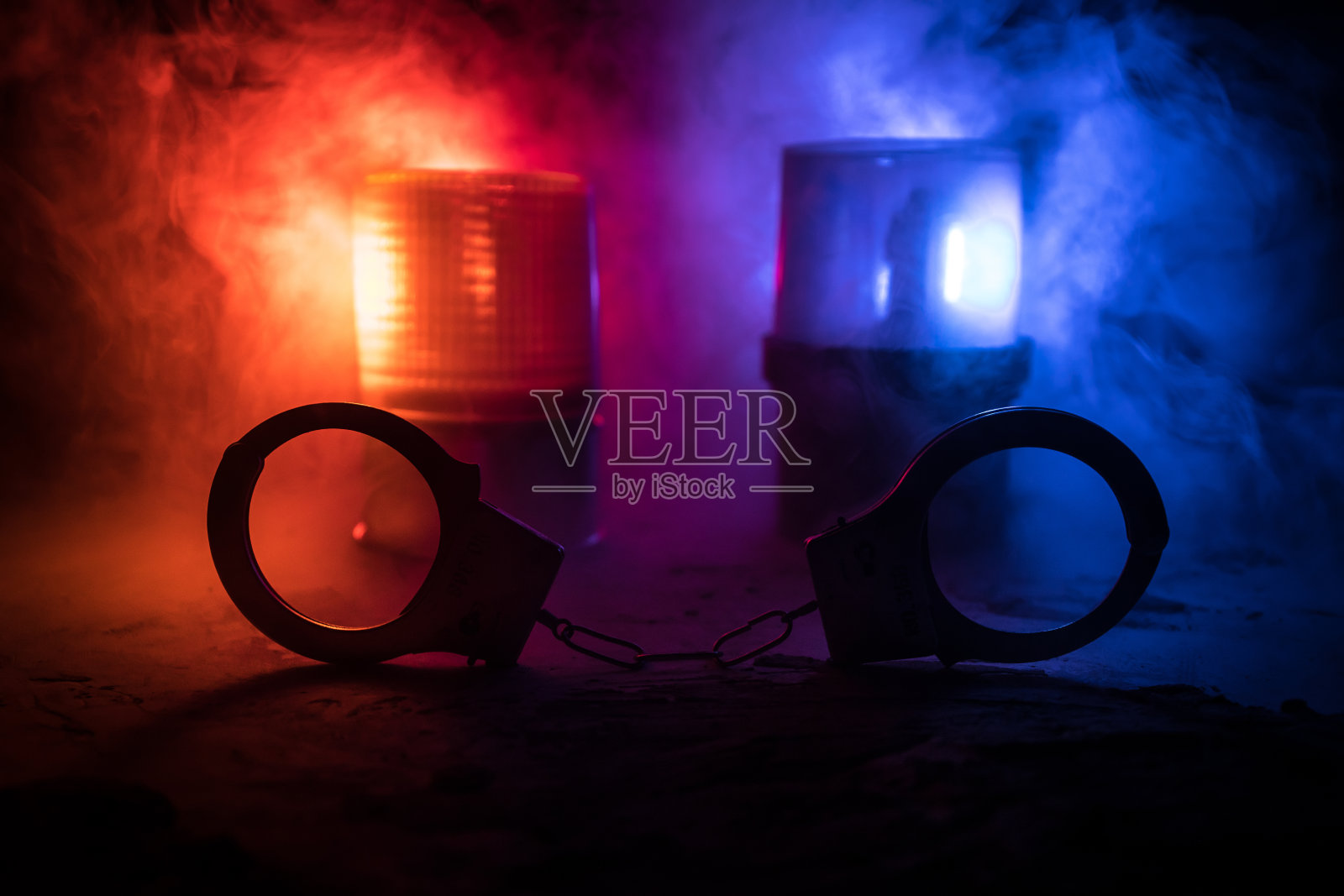 警方夜间突袭,你将被逮捕。手铐的轮廓和警车在后面。在雾蒙蒙的背景下,红色和蓝色警灯闪烁。照片摄影图片