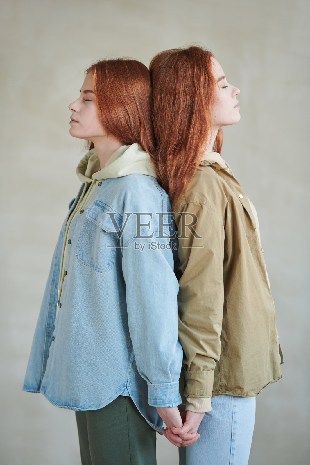 垂直中长侧视工作室肖像两个年轻的红头发的姐妹站在眼睛闭着头,头牵手照片摄影图片