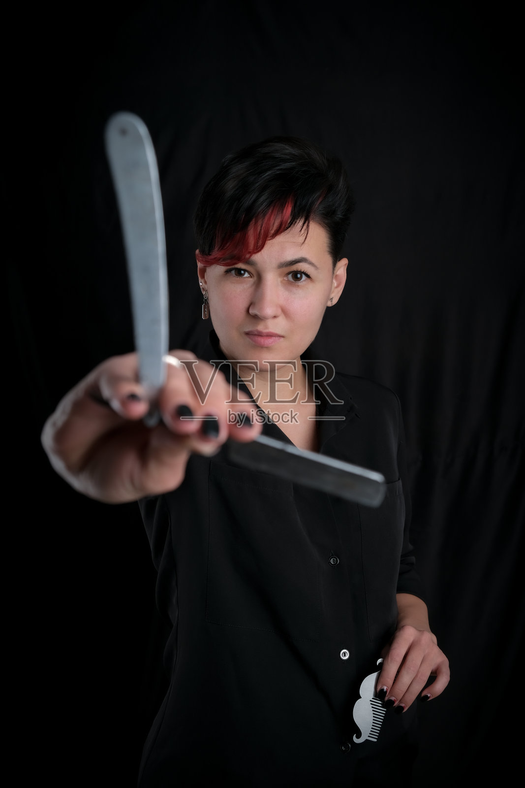 半长的肖像年轻的成年理发师妇女在黑色的背景持有金属胡子形状的梳子和复古直剃刀,现代的理发师女孩的概念照片摄影图片