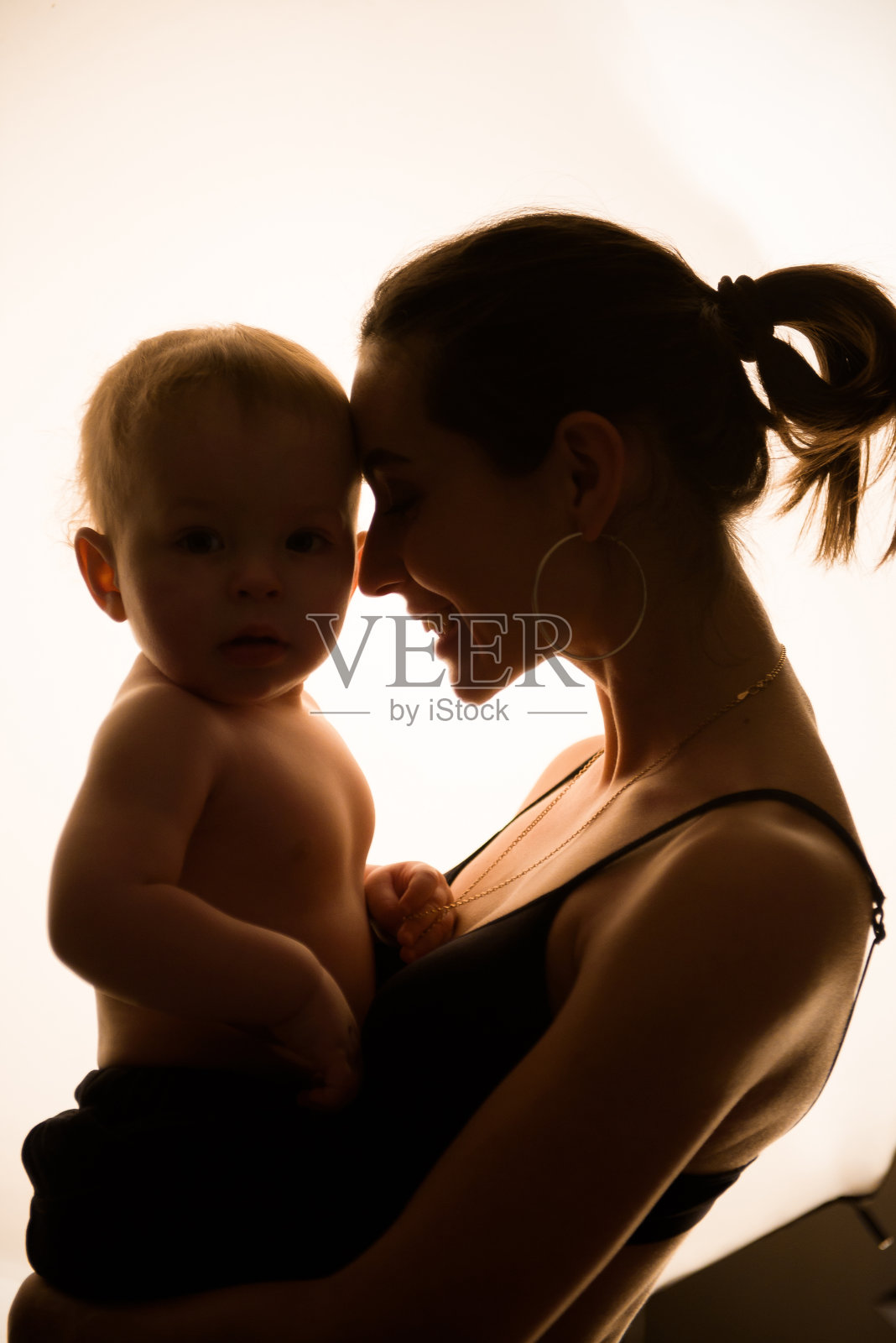 快乐慈爱的年轻母亲亲吻她蹒跚学步的儿子。照片摄影图片