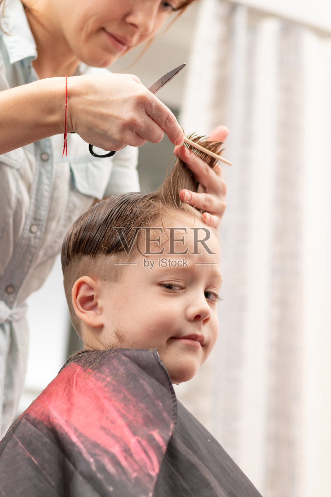 年轻漂亮的妈妈穿着浅蓝色的衣服,手里拿着梳子和剪刀在家给儿子理发。有选择性的重点照片摄影图片