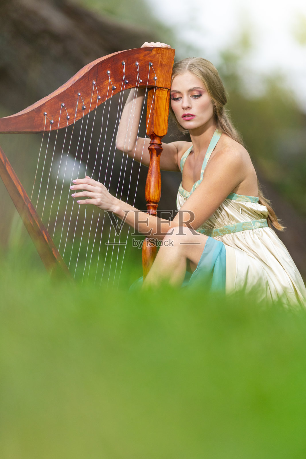 可爱的梦中竖琴师女人穿着轻盈的衣服在户外公园弹奏竖琴。垂直方向照片摄影图片