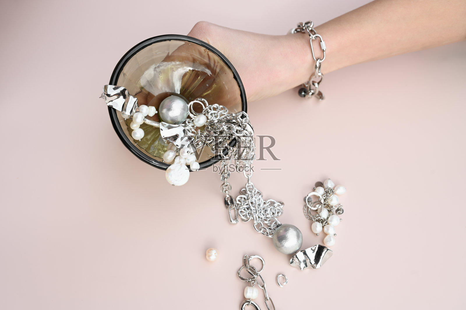 女性手握时尚的玻璃高脚杯,搭配不同的耳环和项链。珠宝展示创意照片摄影图片