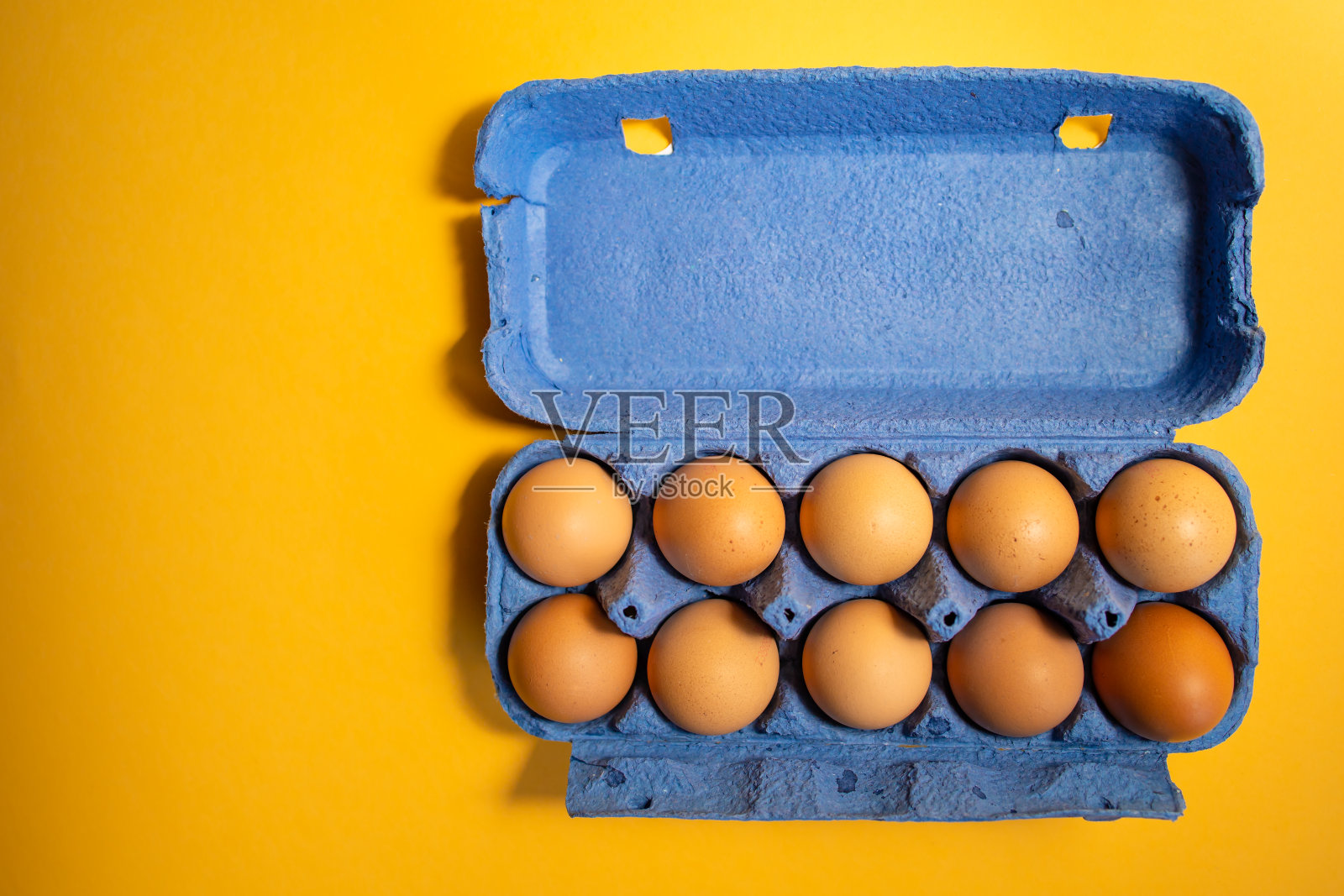 新鲜的鸡蛋放在蓝色的纸盒里,以黄色为底色照片摄影图片