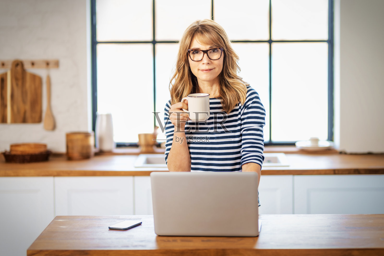 微笑成熟的女人使用她的笔记本电脑和喝咖啡,在家里工作照片摄影图片