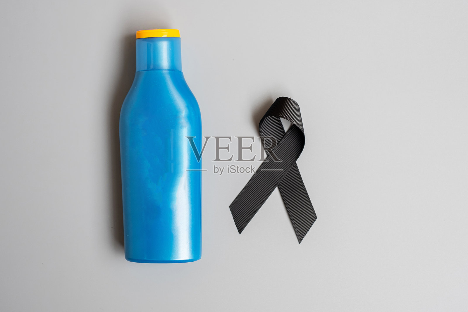 黑色素瘤和皮肤癌宣传月。黑色丝带和身体防晒瓶在灰色的背景。世界癌症日概念照片摄影图片