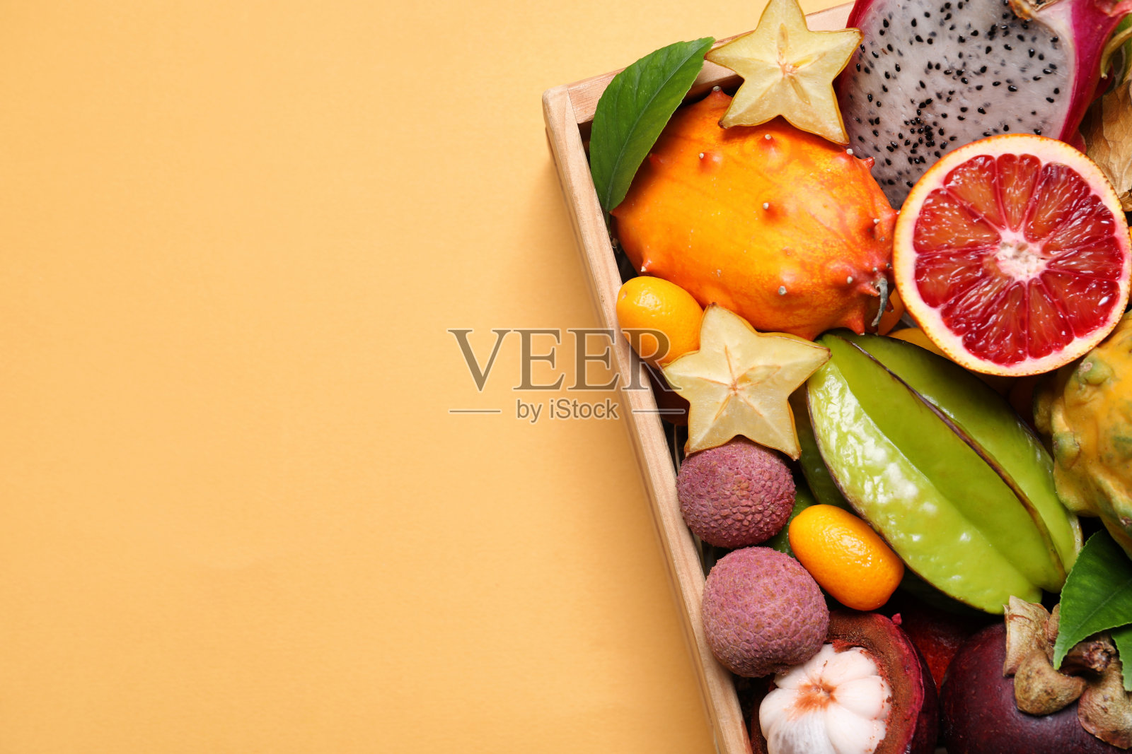 不同的热带水果在木箱黄色背景,俯视图。空间的文本照片摄影图片