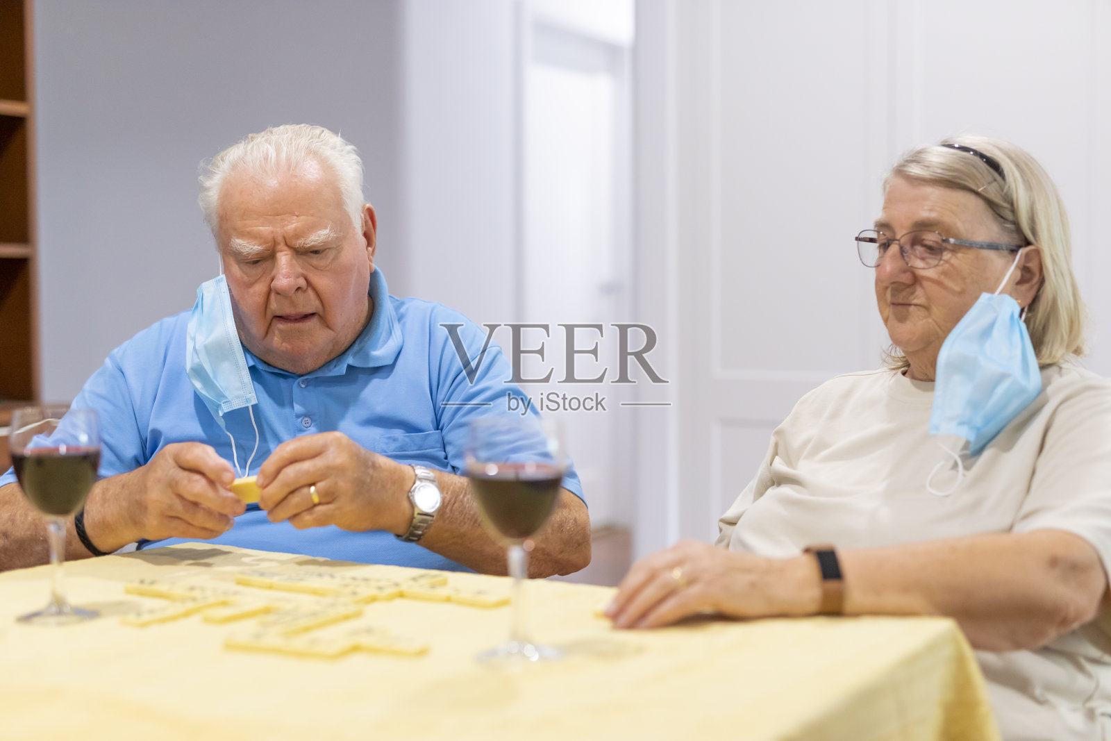戴着冠状病毒面具的老年夫妇一边喝红酒一边玩多米诺骨牌照片摄影图片